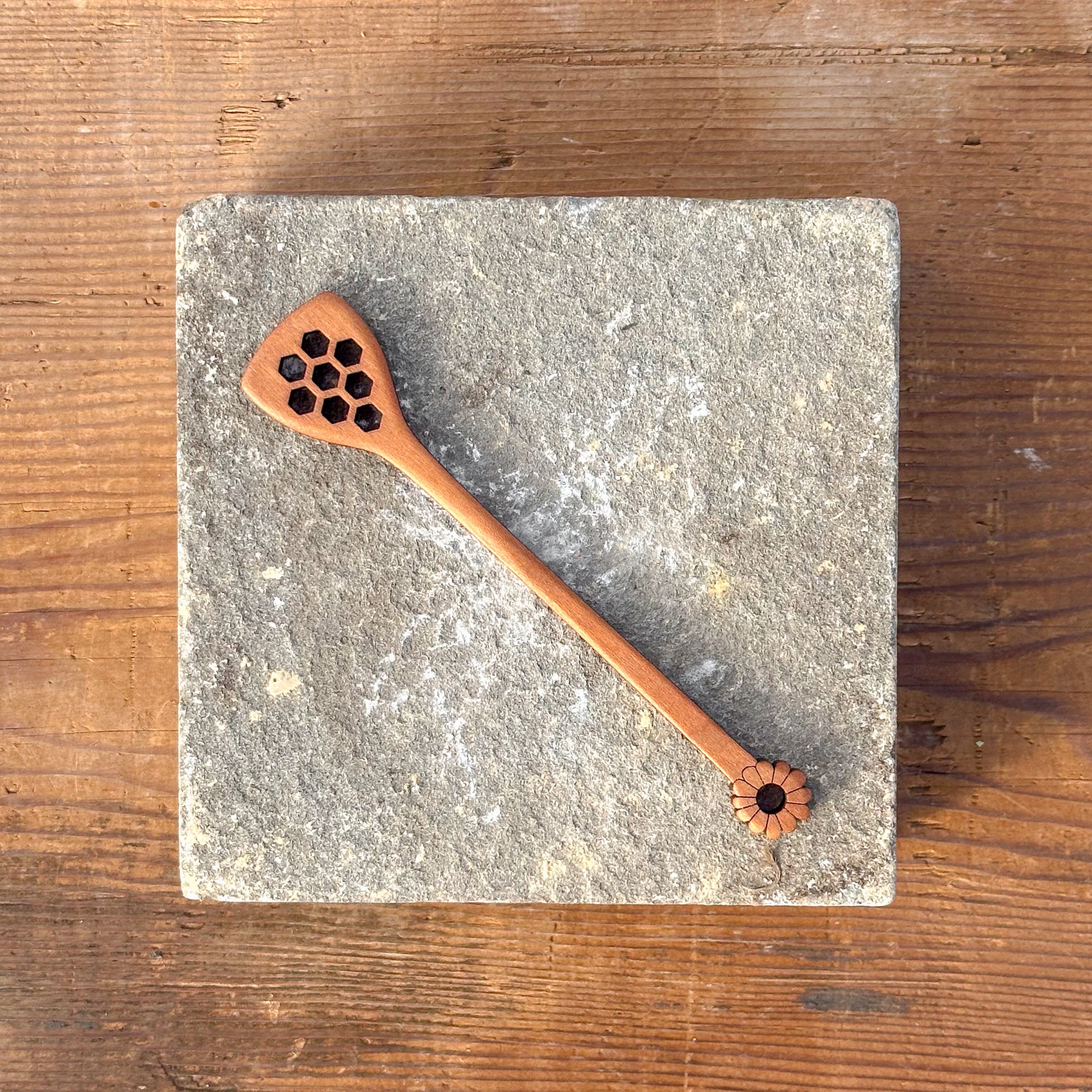 Wooden spoon with decorative holes on a stone coaster, placed on a wooden surface.