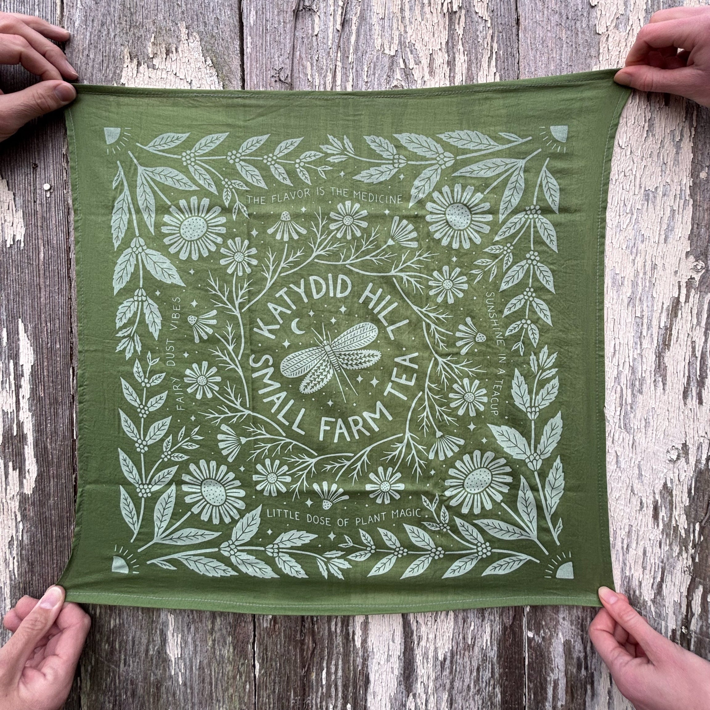 Green fabric with white floral and leaf pattern held by hands on a wooden surface