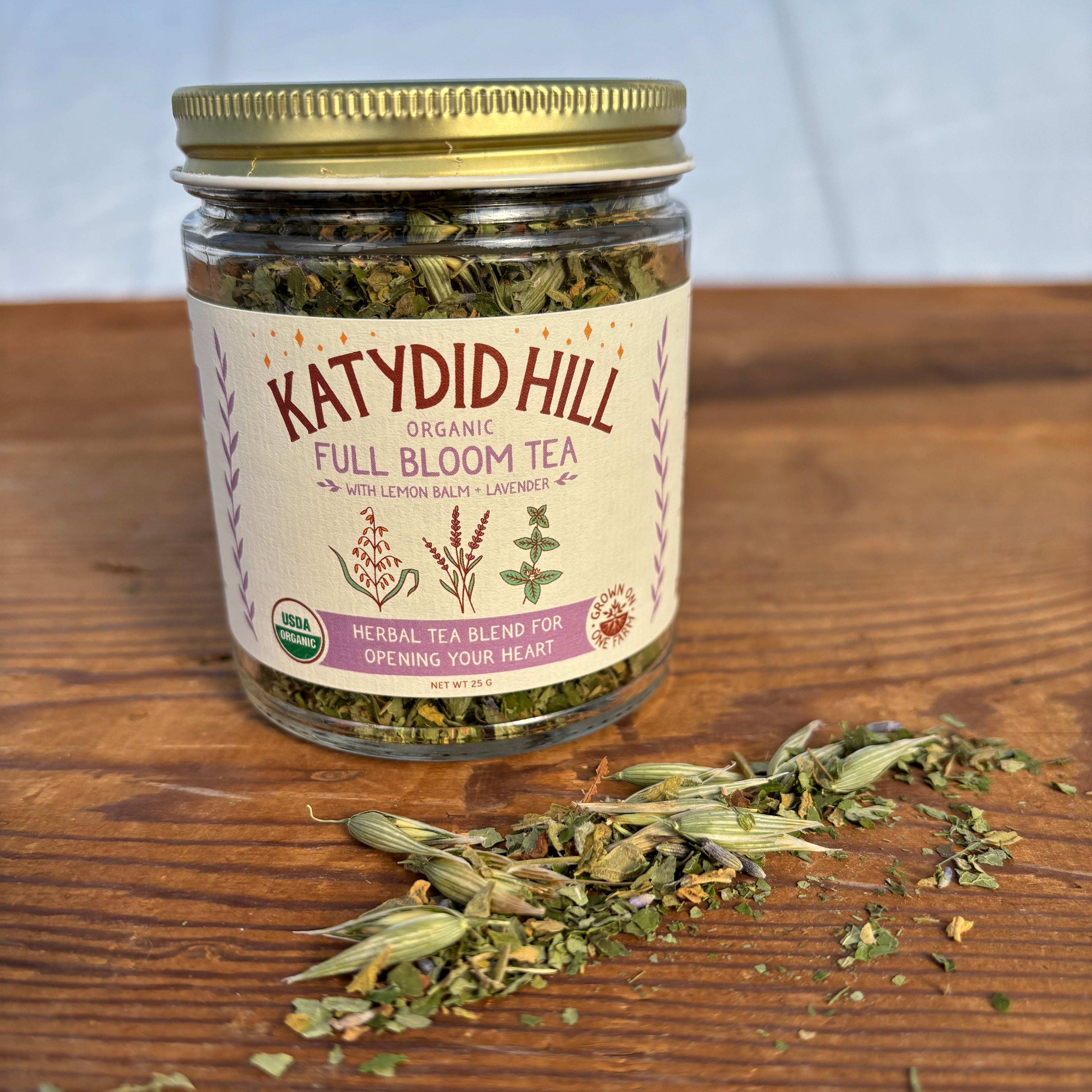 Jar of Katydid Hill Full Bloom Tea on a wooden surface with loose leaf herbal tea.