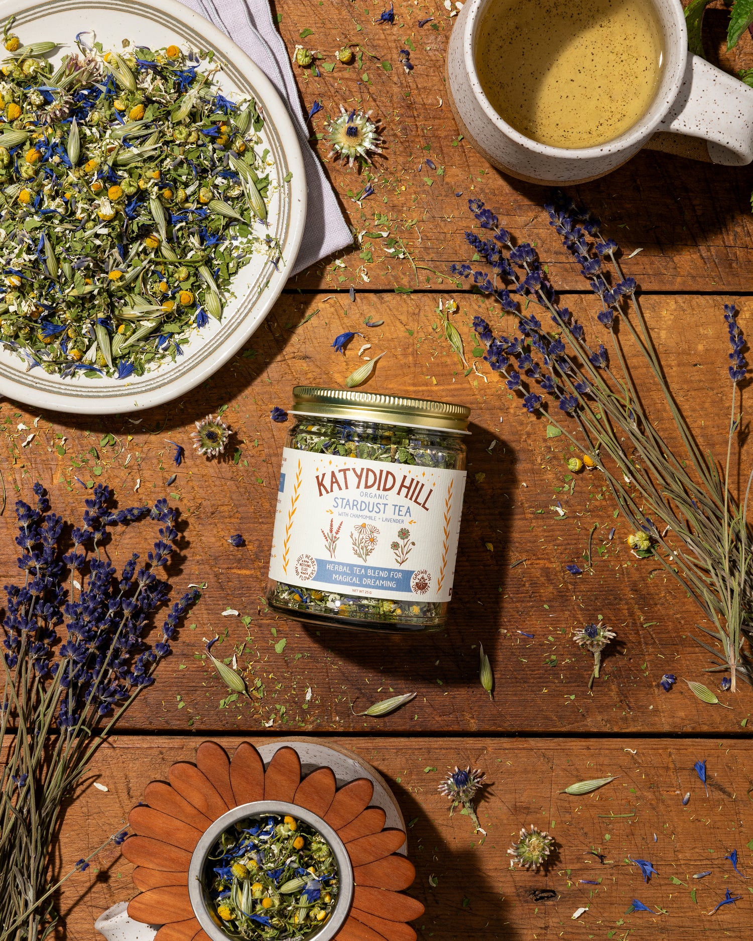 glass jar of stardust tea on wood background with lavender loose herbs and cup of tea