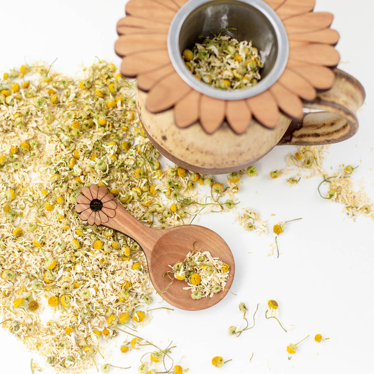 wooden tea scoop with chamomile, ceramic mug, and tea strainer