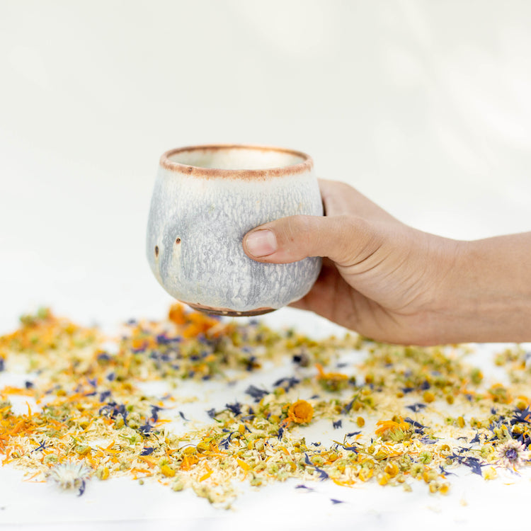 Ceramic tumbler teacup with hand dimples surrounded by loose leaf herbal tea