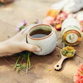 Ceramic tumbler teacup with hand dimples, surrounded by tea scoop, herbal tea glass jar and earthy tones