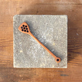 Wooden spoon with decorative holes on a stone coaster, placed on a wooden surface.