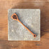 Wooden spoon with decorative holes on a stone coaster, placed on a wooden surface.
