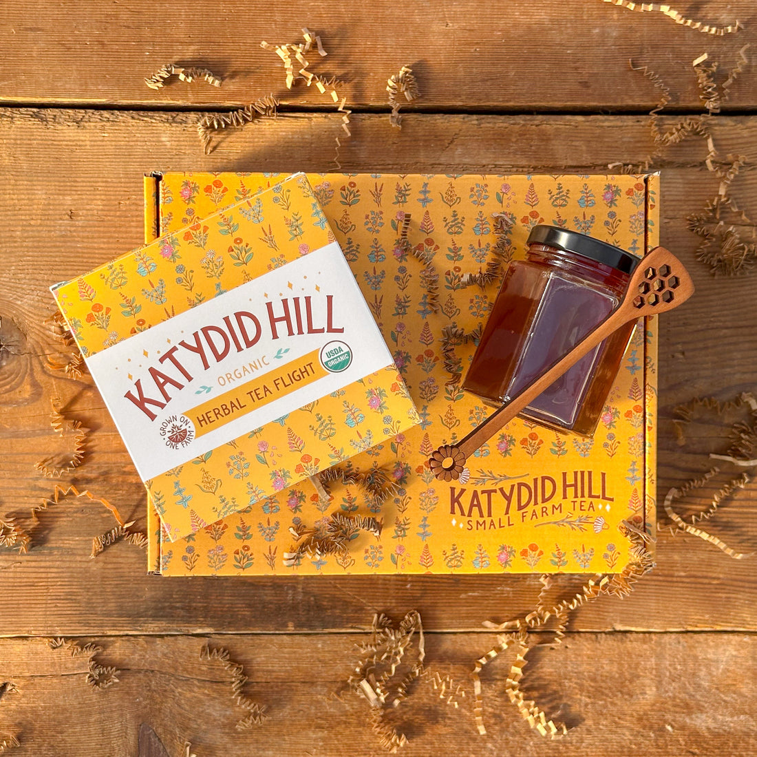 Katydid Hill tea packaging on a wooden surface with a honey jar and spoon.