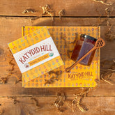 Katydid Hill tea packaging on a wooden surface with a honey jar and spoon.