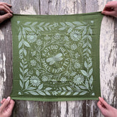 Green fabric with white floral and leaf pattern held by hands on a wooden surface