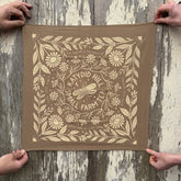 Brown fabric with floral and katydid pattern held by two hands on a wooden surface