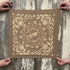 Brown fabric with floral and katydid pattern held by two hands on a wooden surface