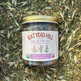 Jar of Katydid Hill Full Bloom Tea on a bed of loose leaf herbal tea