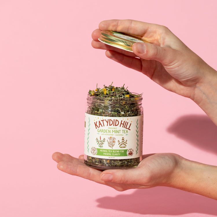 hands holding an open jar of garden mint tea on pink background