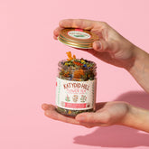 hands holding an open jar of flower tea on pink background