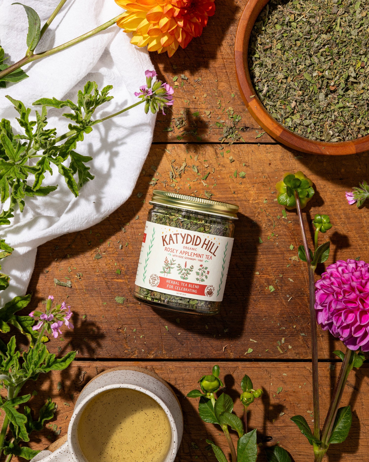 rosey applemint tea on wood background with loose herbs and cup of tea