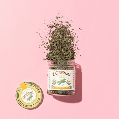 glass jar of tulsi loose leaf tea on to pink background.