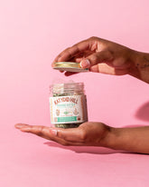 hands holding an open jar of moonbeam tea bags on pink background