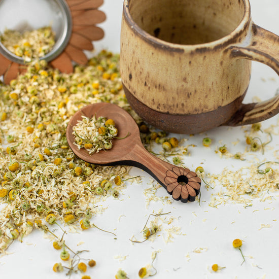 Ceramic mug, wooden tea scoop and tea strainer with loose leaf herbal tea chamomile flowers