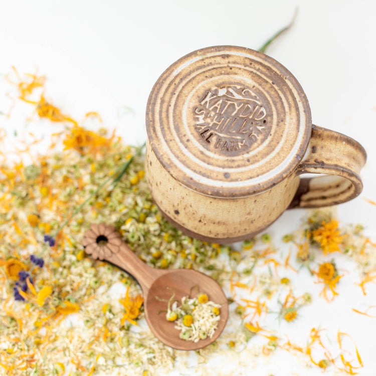 Ceramic mug with lid and wooden tea scoop with loose leaf herbal tea flowers