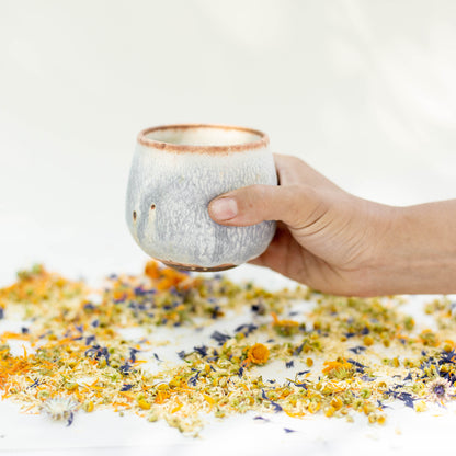 Ceramic tumbler teacup with hand dimples surrounded by loose leaf herbal tea